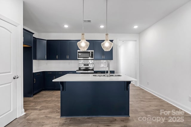 kitchen featuring stainless steel appliances, sink, a center island with sink, and blue cabinetry