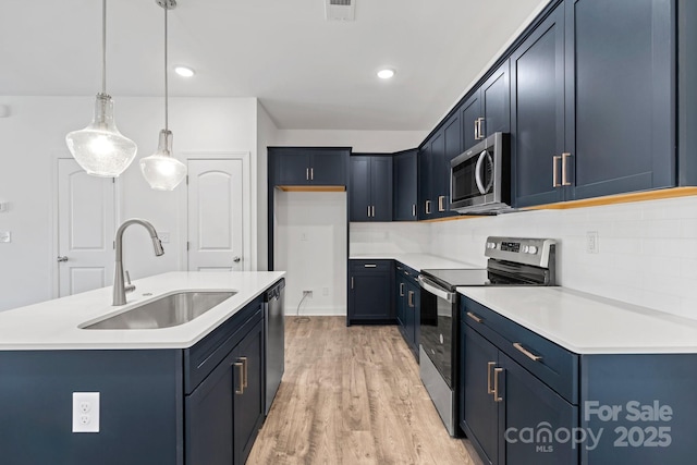 kitchen featuring sink, hanging light fixtures, light hardwood / wood-style flooring, appliances with stainless steel finishes, and an island with sink