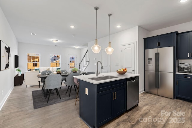 kitchen with pendant lighting, sink, stainless steel appliances, an island with sink, and light wood-type flooring