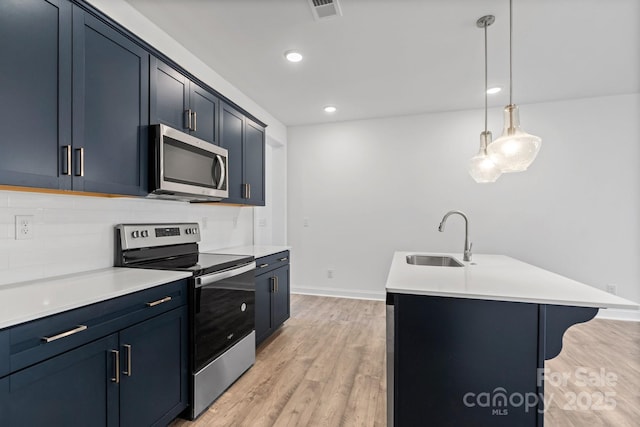 kitchen with sink, a kitchen island with sink, pendant lighting, stainless steel appliances, and light hardwood / wood-style floors