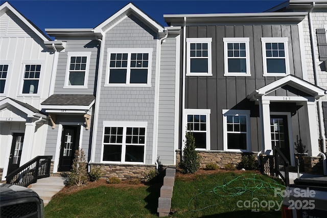 townhome / multi-family property with board and batten siding, a front lawn, and stone siding