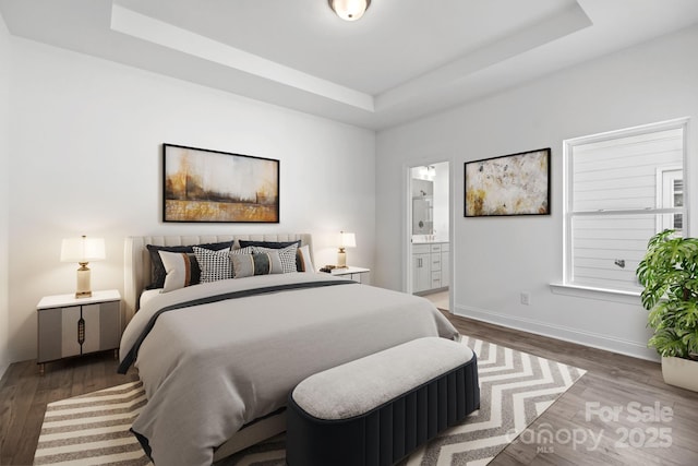bedroom featuring ensuite bath, baseboards, wood finished floors, and a raised ceiling