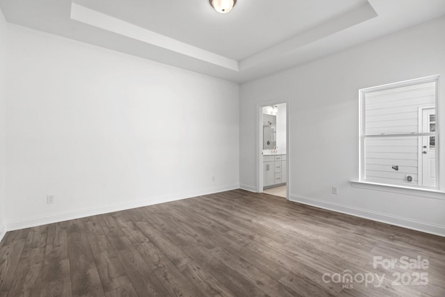 spare room with baseboards, dark wood-style floors, and a raised ceiling