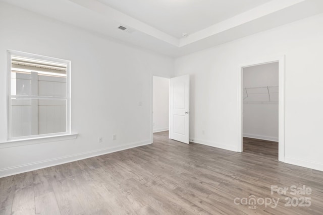 unfurnished bedroom featuring visible vents, baseboards, wood finished floors, a closet, and a walk in closet