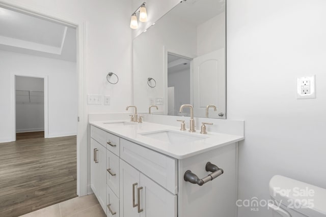 full bath with toilet, double vanity, a sink, and baseboards