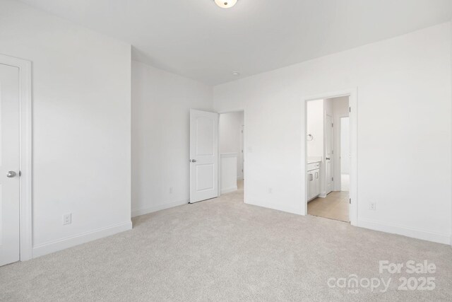 unfurnished bedroom with ensuite bath, light colored carpet, and baseboards