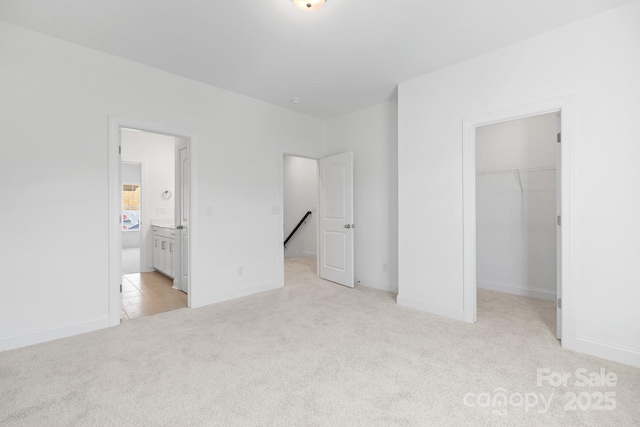 unfurnished bedroom with a spacious closet, light carpet, a closet, baseboards, and ensuite bathroom