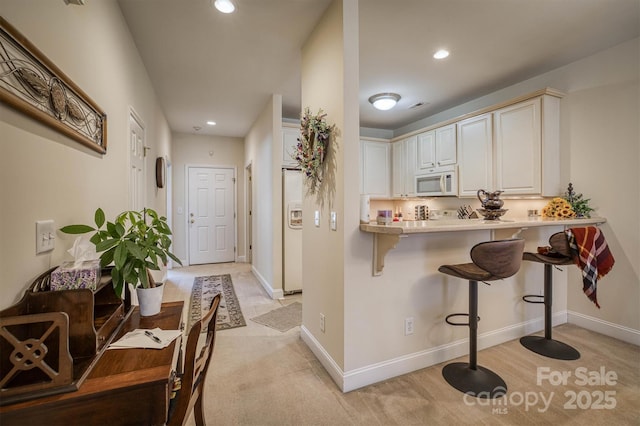 kitchen with white appliances, white cabinetry, light colored carpet, kitchen peninsula, and a breakfast bar area