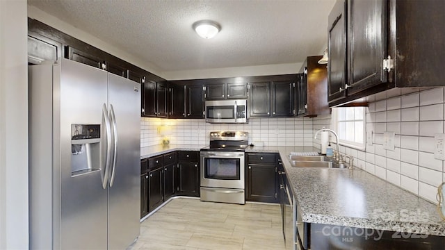 kitchen with sink, tasteful backsplash, a textured ceiling, dark brown cabinets, and appliances with stainless steel finishes