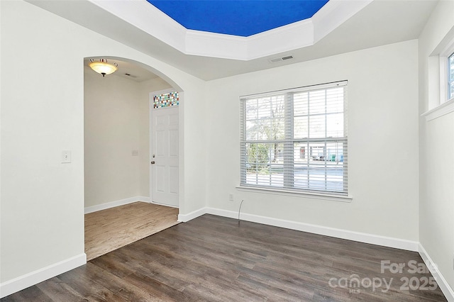 empty room featuring dark hardwood / wood-style floors, ornamental molding, and a tray ceiling