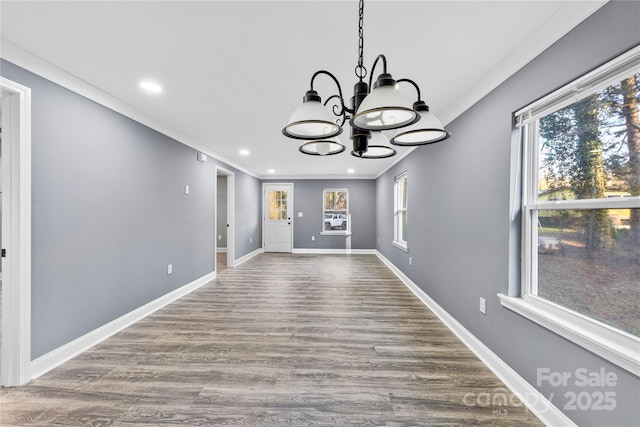 unfurnished dining area featuring hardwood / wood-style flooring, an inviting chandelier, a wealth of natural light, and ornamental molding