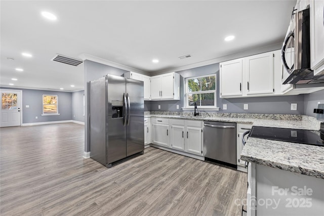 kitchen with white cabinets, crown molding, sink, appliances with stainless steel finishes, and light hardwood / wood-style floors