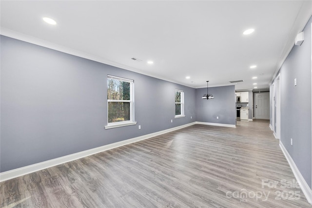 unfurnished living room featuring a chandelier, light wood-type flooring, and ornamental molding