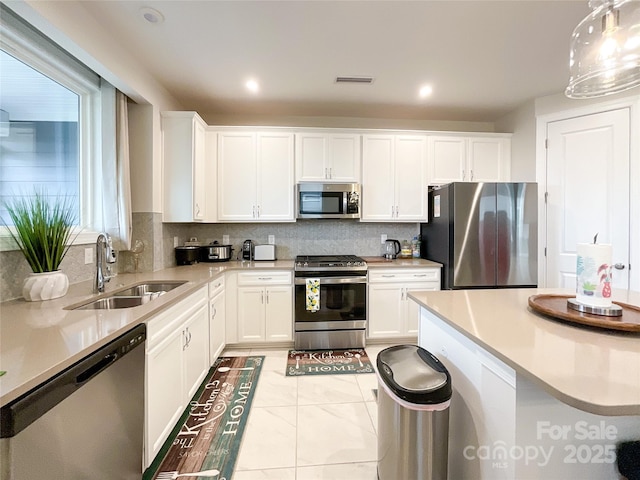 kitchen featuring sink, light tile patterned floors, decorative light fixtures, white cabinetry, and stainless steel appliances