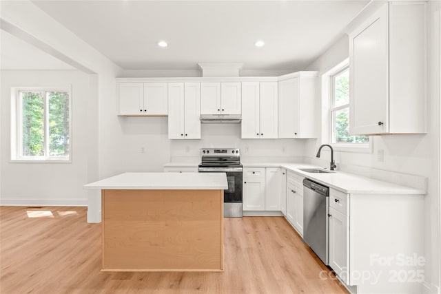 kitchen featuring appliances with stainless steel finishes, light wood-type flooring, sink, a center island, and white cabinetry