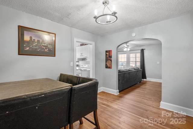 dining space featuring ceiling fan with notable chandelier, a textured ceiling, and light hardwood / wood-style flooring