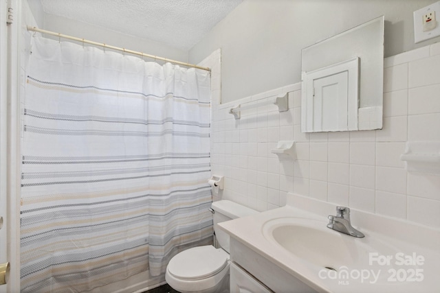 bathroom featuring a textured ceiling, vanity, toilet, and tile walls