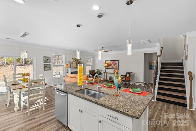 kitchen with a kitchen island with sink, sink, stainless steel dishwasher, ornamental molding, and white cabinetry