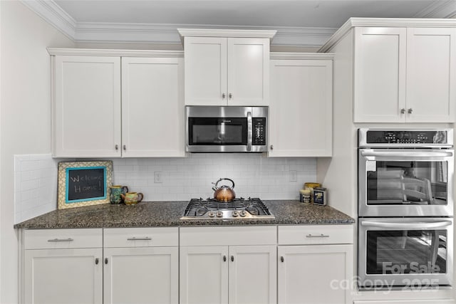 kitchen featuring stainless steel appliances, dark stone counters, decorative backsplash, white cabinets, and ornamental molding