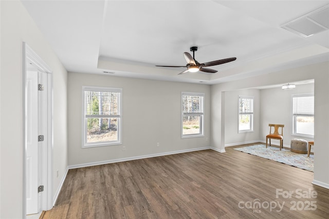 spare room with a tray ceiling, plenty of natural light, dark wood-type flooring, and ceiling fan