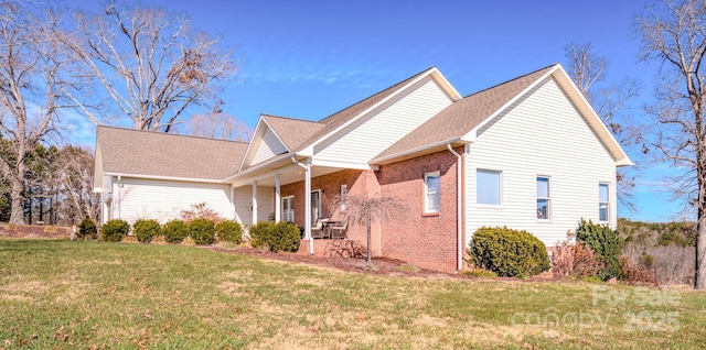 view of side of property with covered porch, a yard, and brick siding