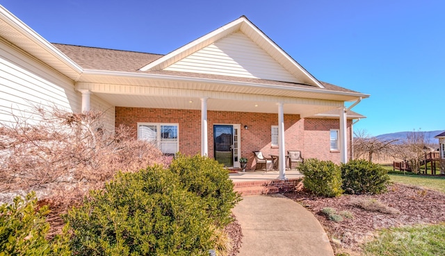 property entrance featuring covered porch, a shingled roof, a mountain view, and brick siding