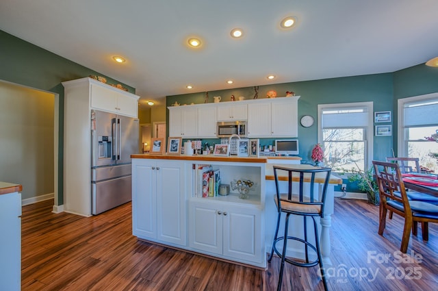 kitchen with appliances with stainless steel finishes, a kitchen island with sink, white cabinets, and dark wood finished floors