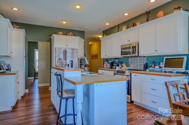 kitchen featuring a center island with sink, white cabinets, dark wood finished floors, appliances with stainless steel finishes, and light countertops