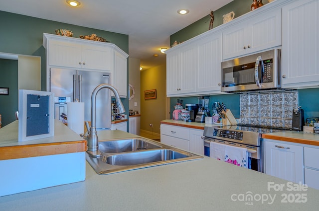 kitchen featuring white cabinets, stainless steel appliances, light countertops, a sink, and recessed lighting