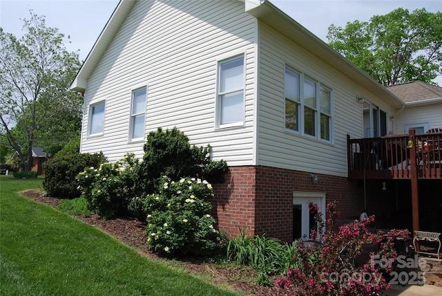 view of side of property with brick siding, a lawn, and a wooden deck