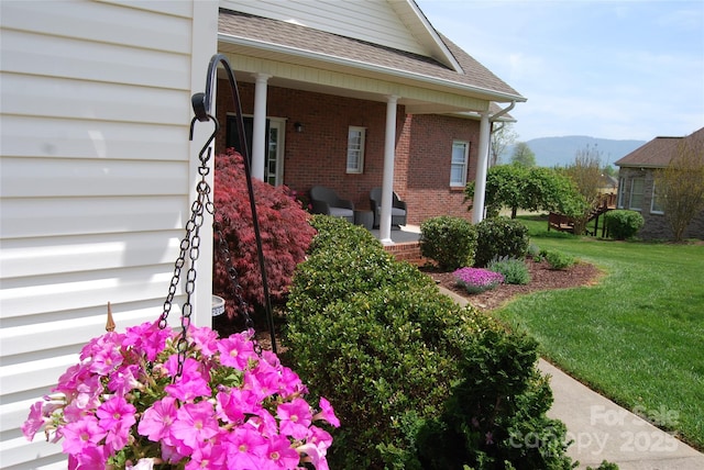 view of exterior entry with a mountain view, a porch, a yard, brick siding, and roof with shingles
