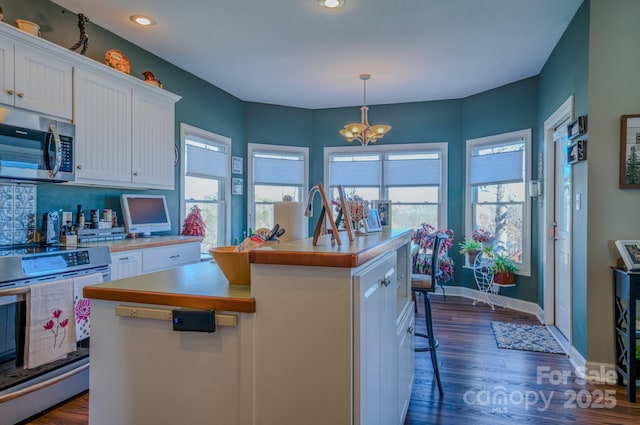 kitchen with range with electric cooktop, an island with sink, light countertops, stainless steel microwave, and white cabinetry