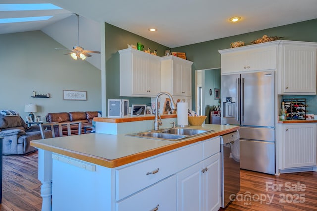 kitchen with stainless steel appliances, wood finished floors, a sink, open floor plan, and white cabinetry