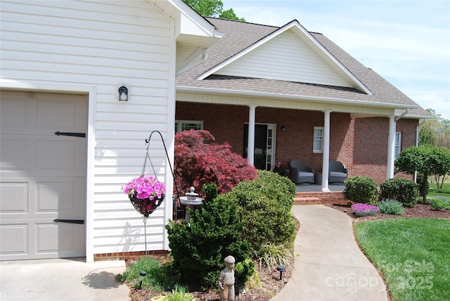 entrance to property with brick siding, roof with shingles, a garage, and covered porch