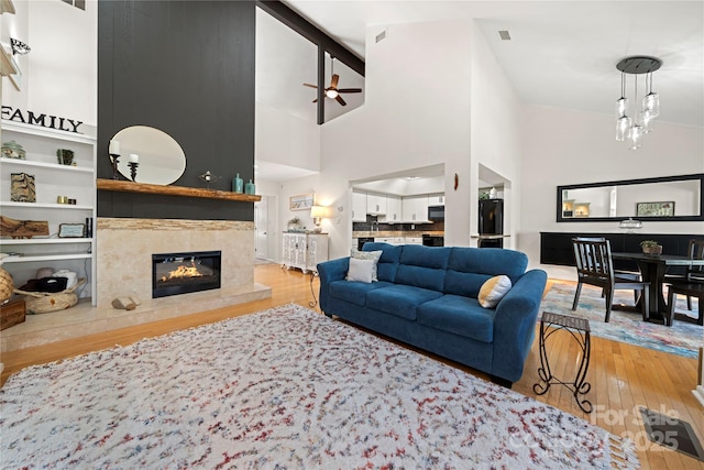 living room with ceiling fan, a high ceiling, light wood-type flooring, and a fireplace