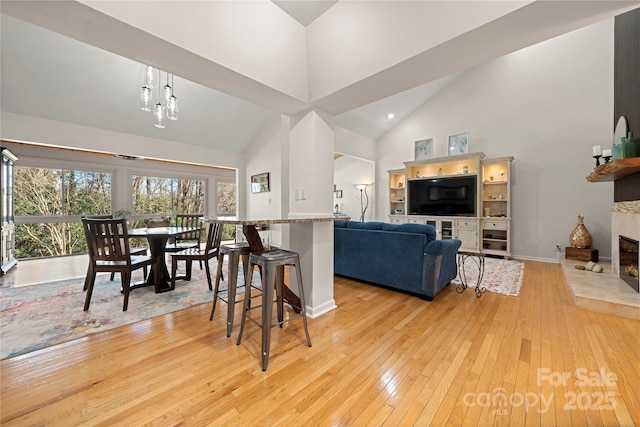 interior space featuring high vaulted ceiling, light wood-type flooring, a tile fireplace, and an inviting chandelier