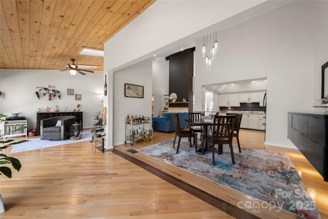 dining room featuring a skylight, ceiling fan, high vaulted ceiling, wooden ceiling, and light hardwood / wood-style flooring