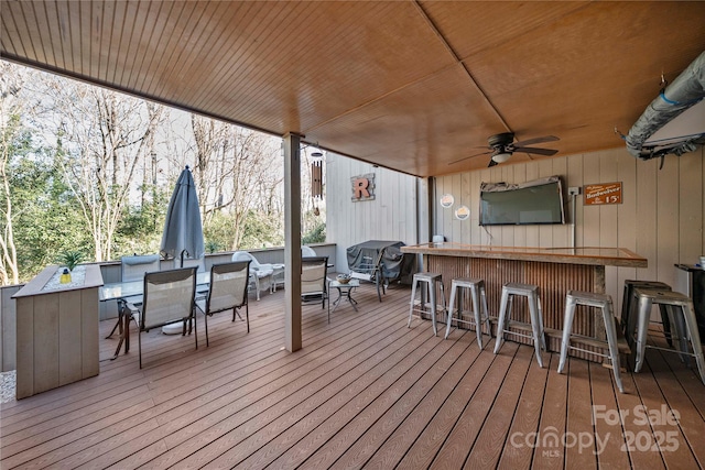 deck featuring ceiling fan and a bar