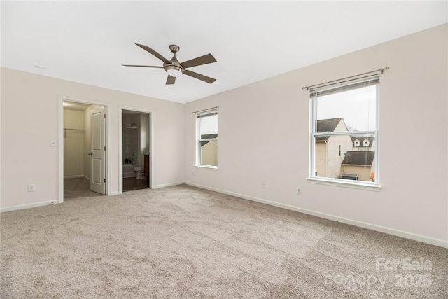 unfurnished bedroom featuring a walk in closet, ensuite bath, a closet, ceiling fan, and carpet