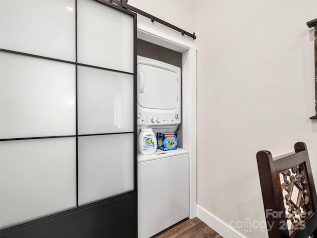 clothes washing area with dark hardwood / wood-style floors, stacked washing maching and dryer, and a barn door