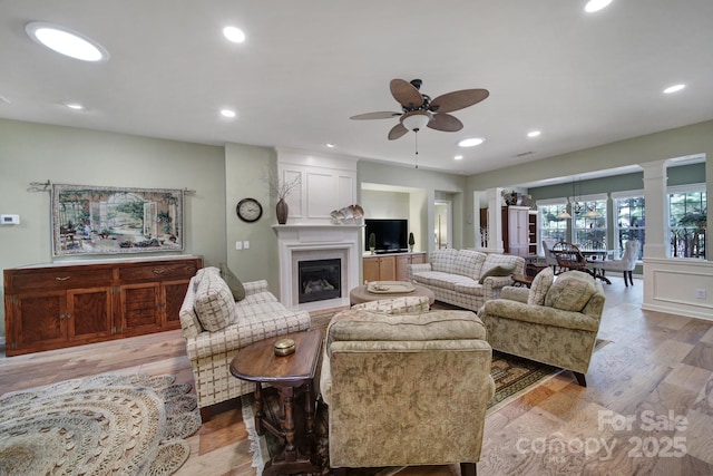 living room with a large fireplace, light hardwood / wood-style floors, and ceiling fan