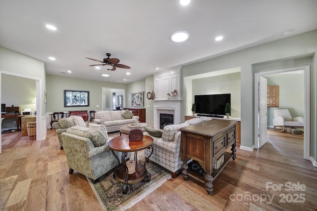 living room featuring a fireplace, ceiling fan, and light hardwood / wood-style flooring