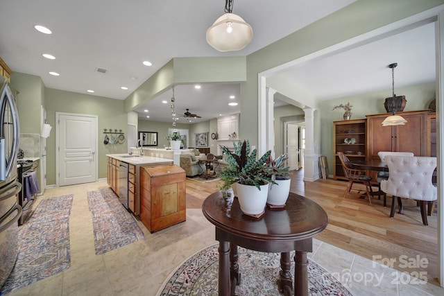 kitchen with a kitchen island with sink, sink, ceiling fan, decorative light fixtures, and stainless steel appliances