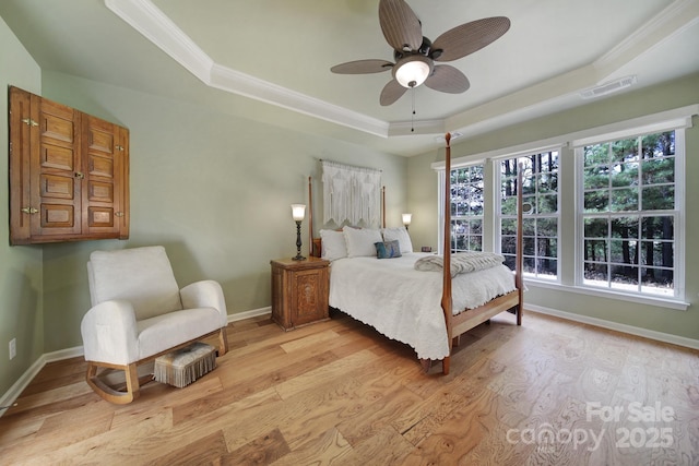 bedroom featuring ceiling fan, light hardwood / wood-style floors, and a tray ceiling