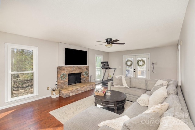 living room with a stone fireplace, ceiling fan, dark hardwood / wood-style flooring, and a healthy amount of sunlight