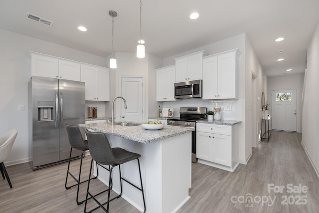 kitchen featuring a center island with sink, stainless steel appliances, pendant lighting, white cabinets, and sink