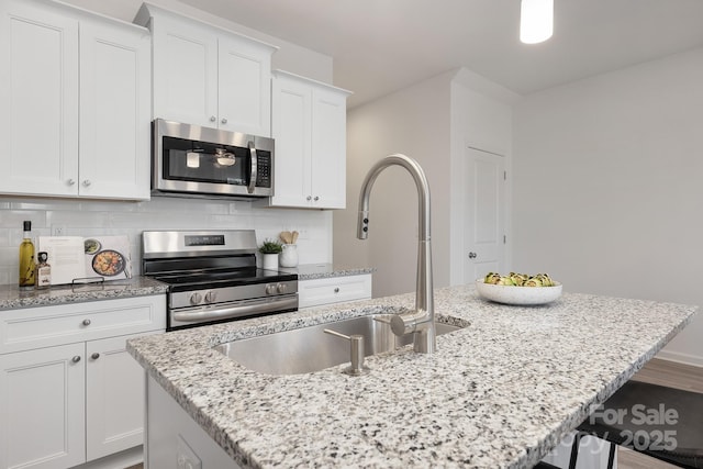 kitchen featuring stainless steel appliances, an island with sink, white cabinetry, and tasteful backsplash