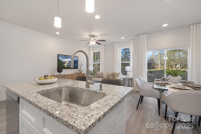 kitchen with light hardwood / wood-style floors, pendant lighting, light stone counters, sink, and white cabinetry