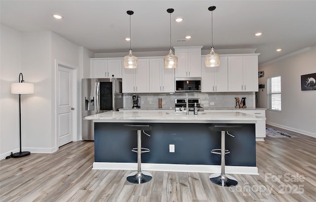 kitchen featuring white cabinets, appliances with stainless steel finishes, decorative light fixtures, and a kitchen island with sink