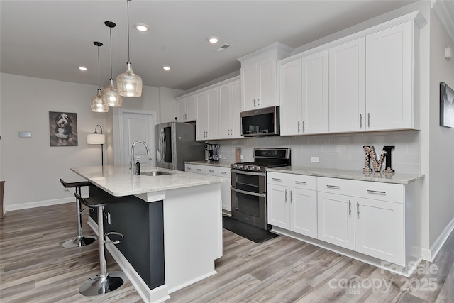 kitchen with backsplash, an island with sink, decorative light fixtures, white cabinetry, and stainless steel appliances